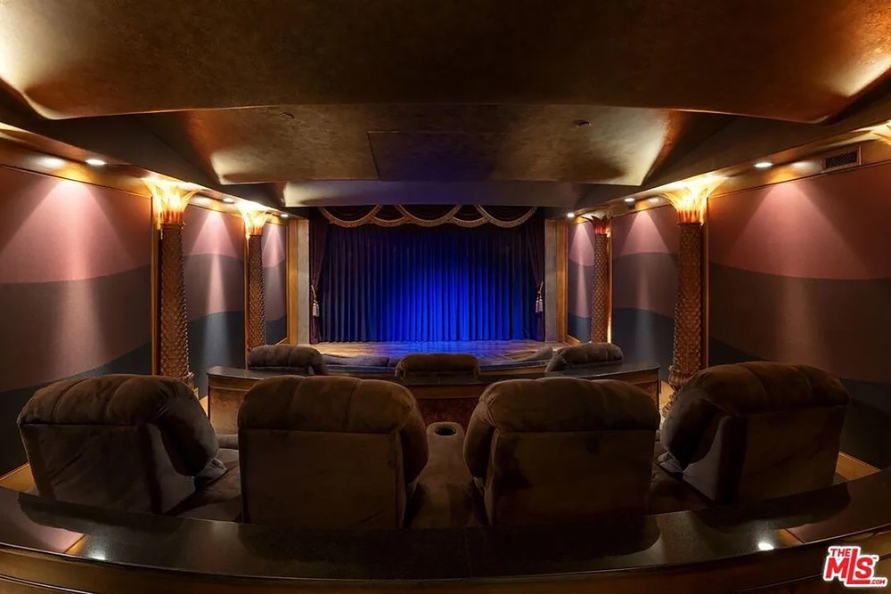 Private home theater room equipped with plush tiered recliner seating and a classic blue curtain stage.
