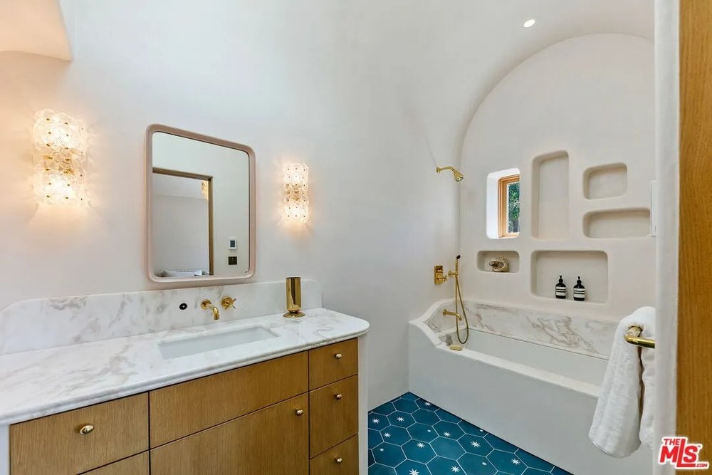 A detailed view of a spa-like bathroom featuring a fluted wood vanity with marble top, distinct built-in shower niches, and striking blue patterned floor tiles.