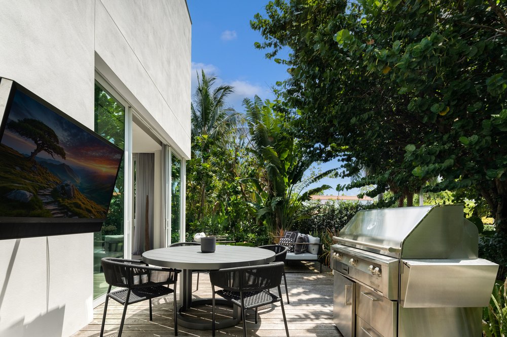 An outdoor patio area with a wooden deck, a dining table, and a large professional-grade stainless steel grill.