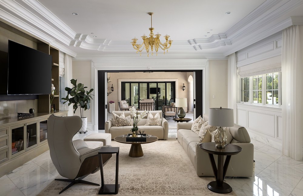 Spacious open-concept family room with a coffered tray ceiling, plush seating, a gold chandelier, and pocket doors opening to the patio.