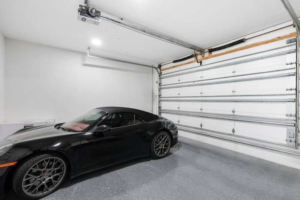 Interior of a clean white garage with a speckled epoxy floor and a black luxury Porsche sports car parked inside.