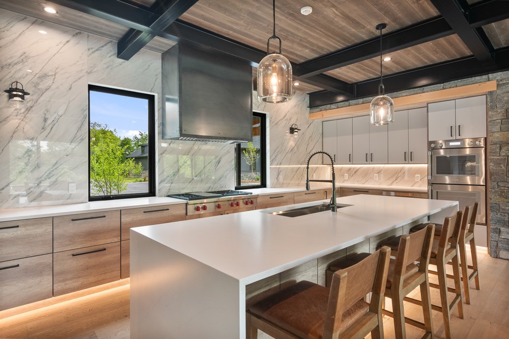 Gourmet kitchen with marble wall tiles, a large waterfall island, stainless steel appliances, and under-cabinet lighting.