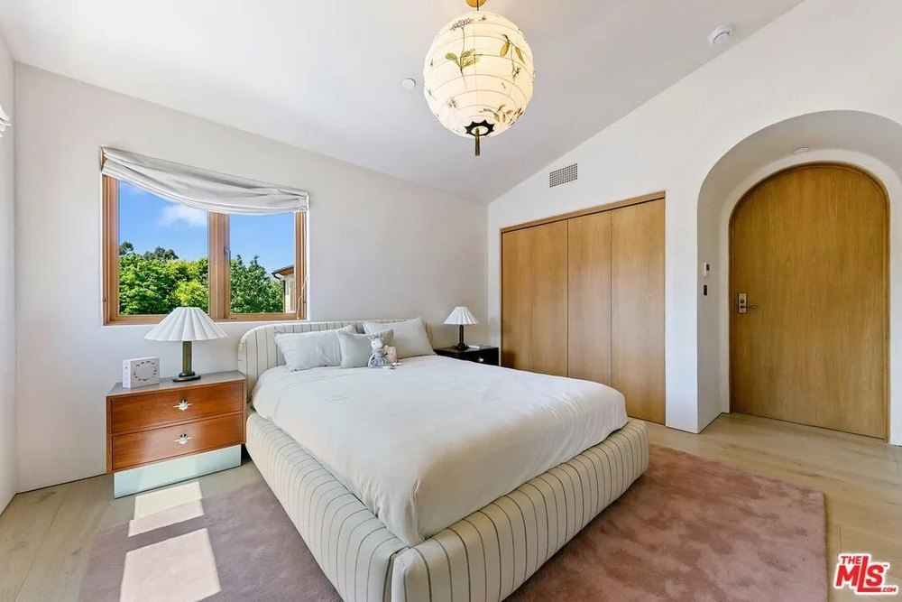 bright bedroom features a striped upholstered bed frame, a pink area rug, and an arched wooden door.