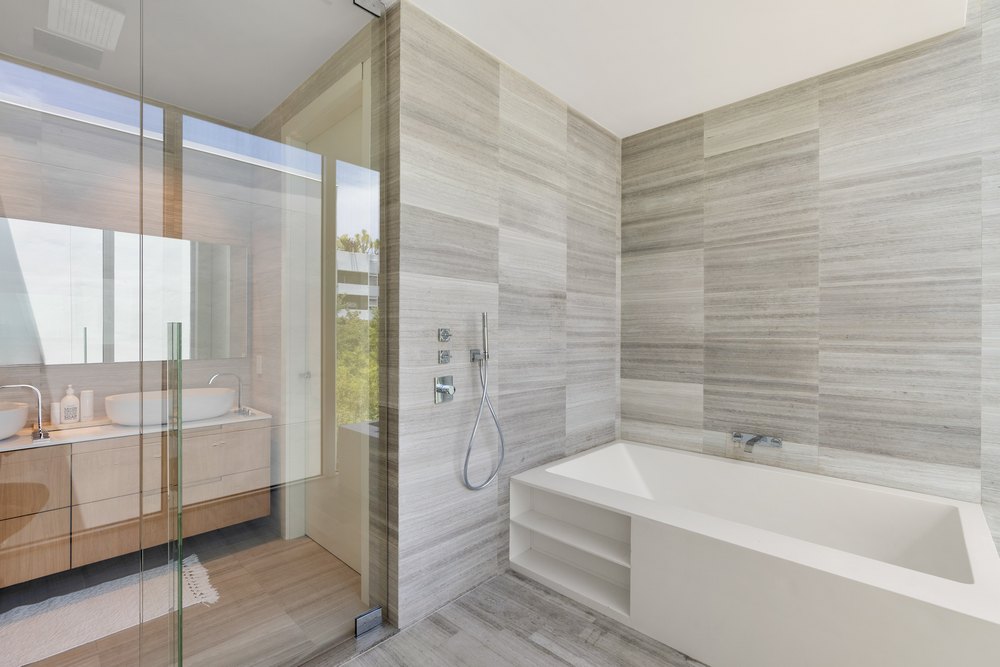 A luxurious bathroom featuring a large white soaking tub and a glass-enclosed shower area with textured stone walls.