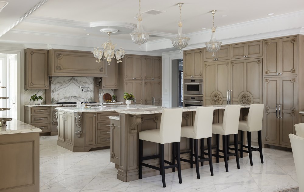 Luxury custom kitchen with ornate beige cabinetry, dual marble-topped islands, a breakfast bar, and hanging glass pendant lights.