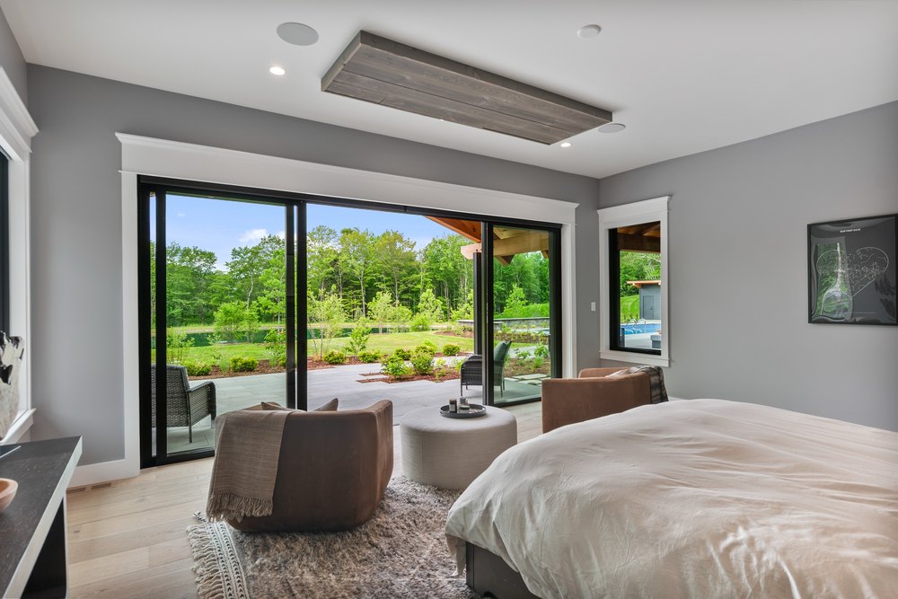 Spacious bedroom lounge area with armchairs, an ottoman, and direct patio access through black-framed sliding glass doors.
