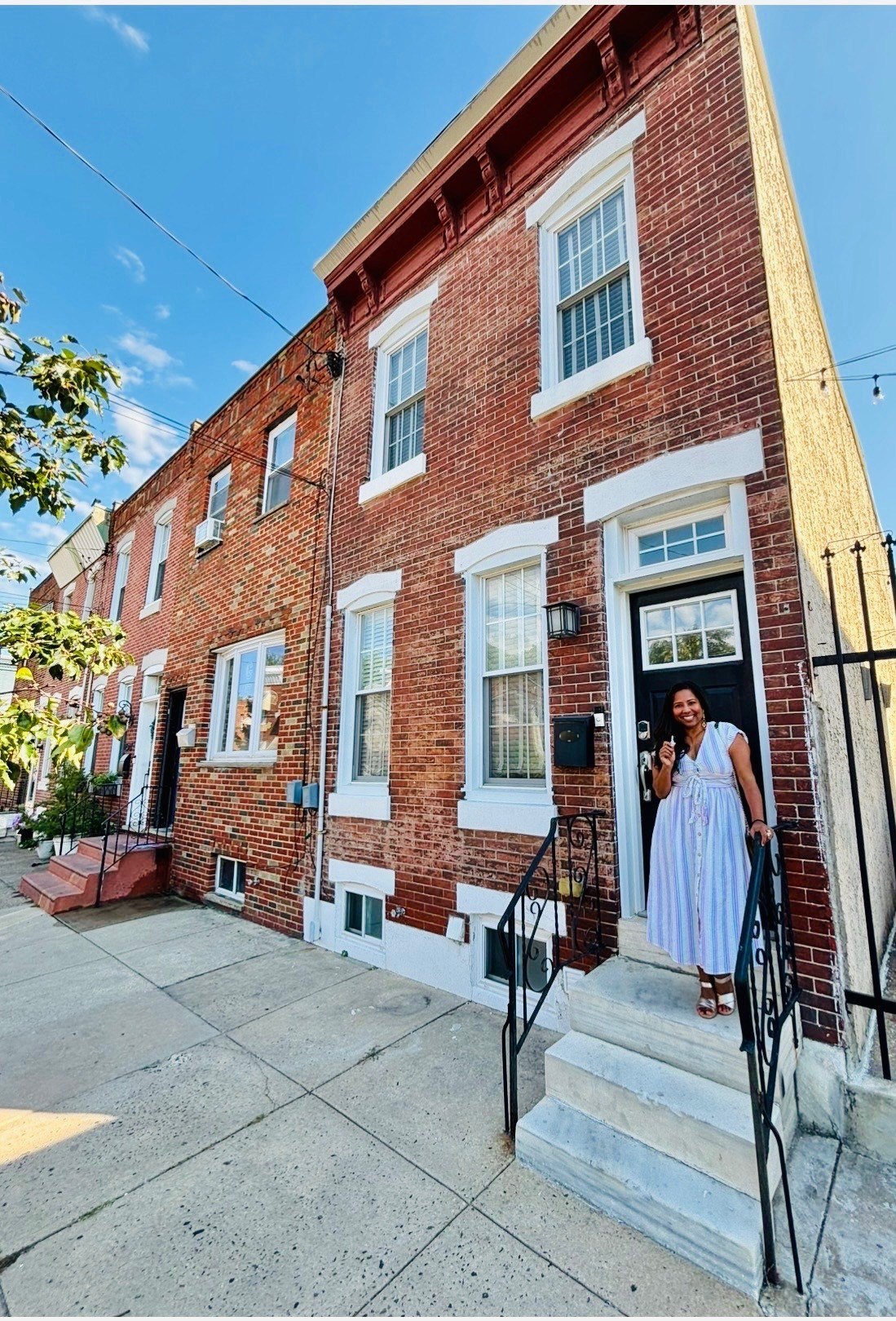 Woman poses with keys in front of row house.