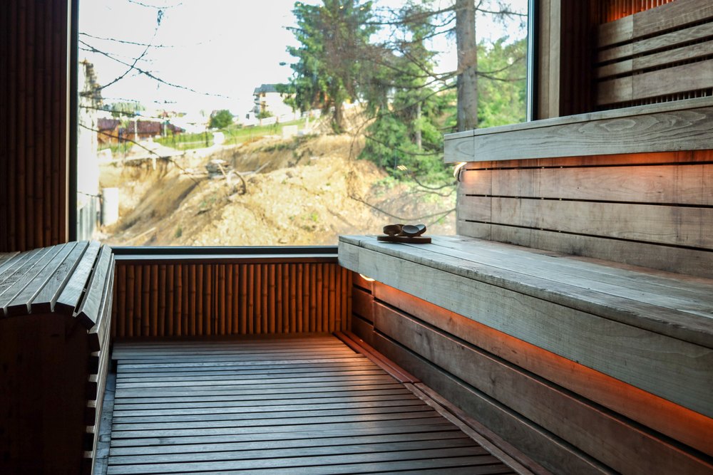 Modern wooden sauna interior with large window overlooking nature. Empty wooden benches, soft lighting and natural design elements create cozy atmosphere for relaxation and wellness.