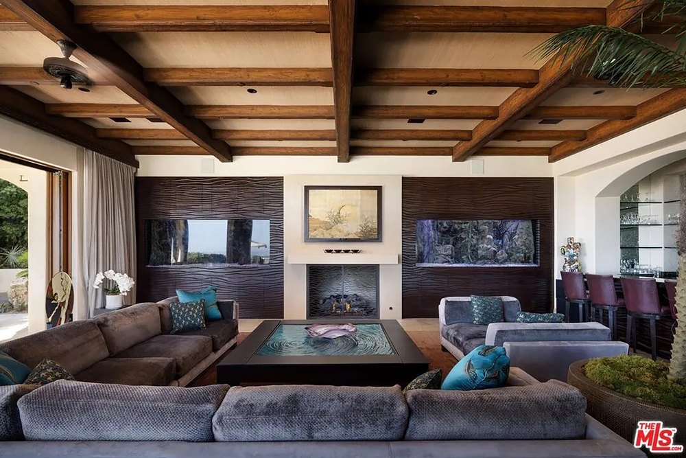 Opulent living room featuring built-in wall aquariums, a cozy fireplace, and an exposed beam ceiling.