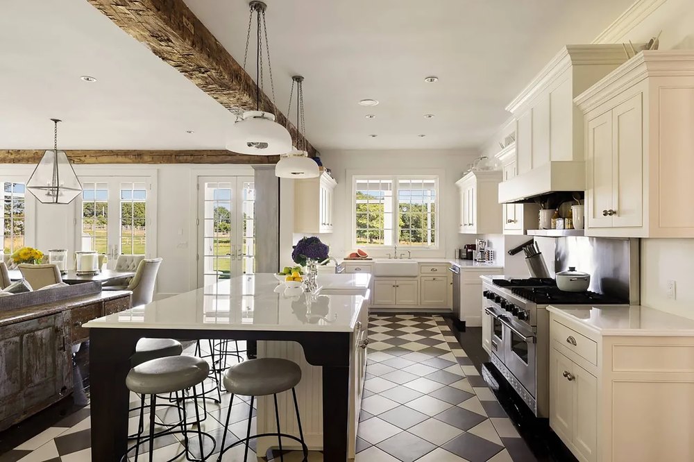 Traditional gourmet kitchen featuring white shaker cabinetry, a black prep island with white marble top, black-and-white checkered tile floors, and a professional stainless steel range.