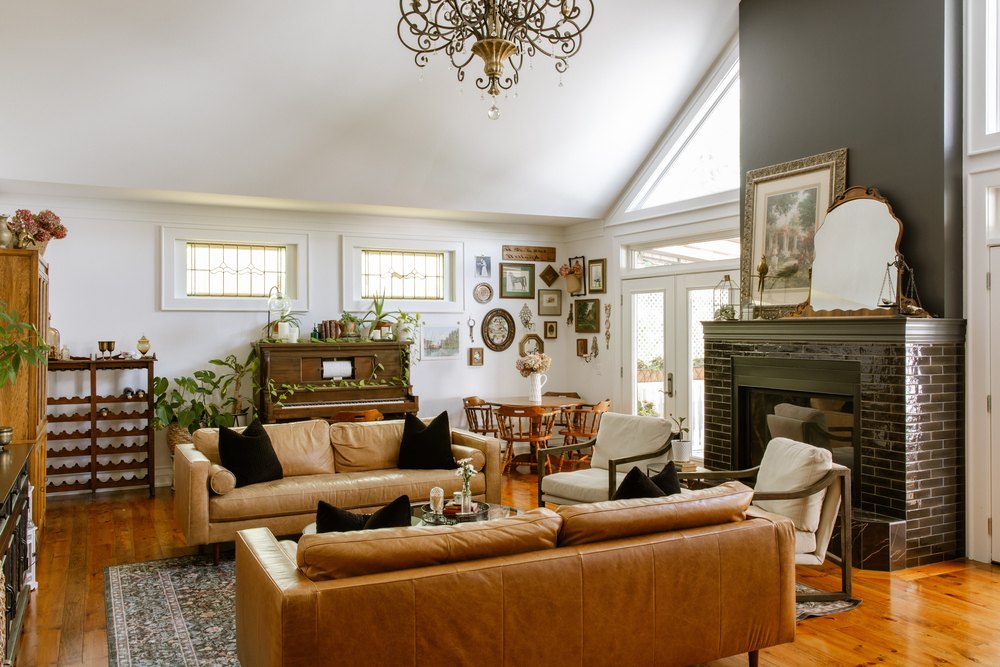 Spacious open-concept living room featuring tan leather sofas, a dark brick fireplace, high ceilings, and a dining alcove.