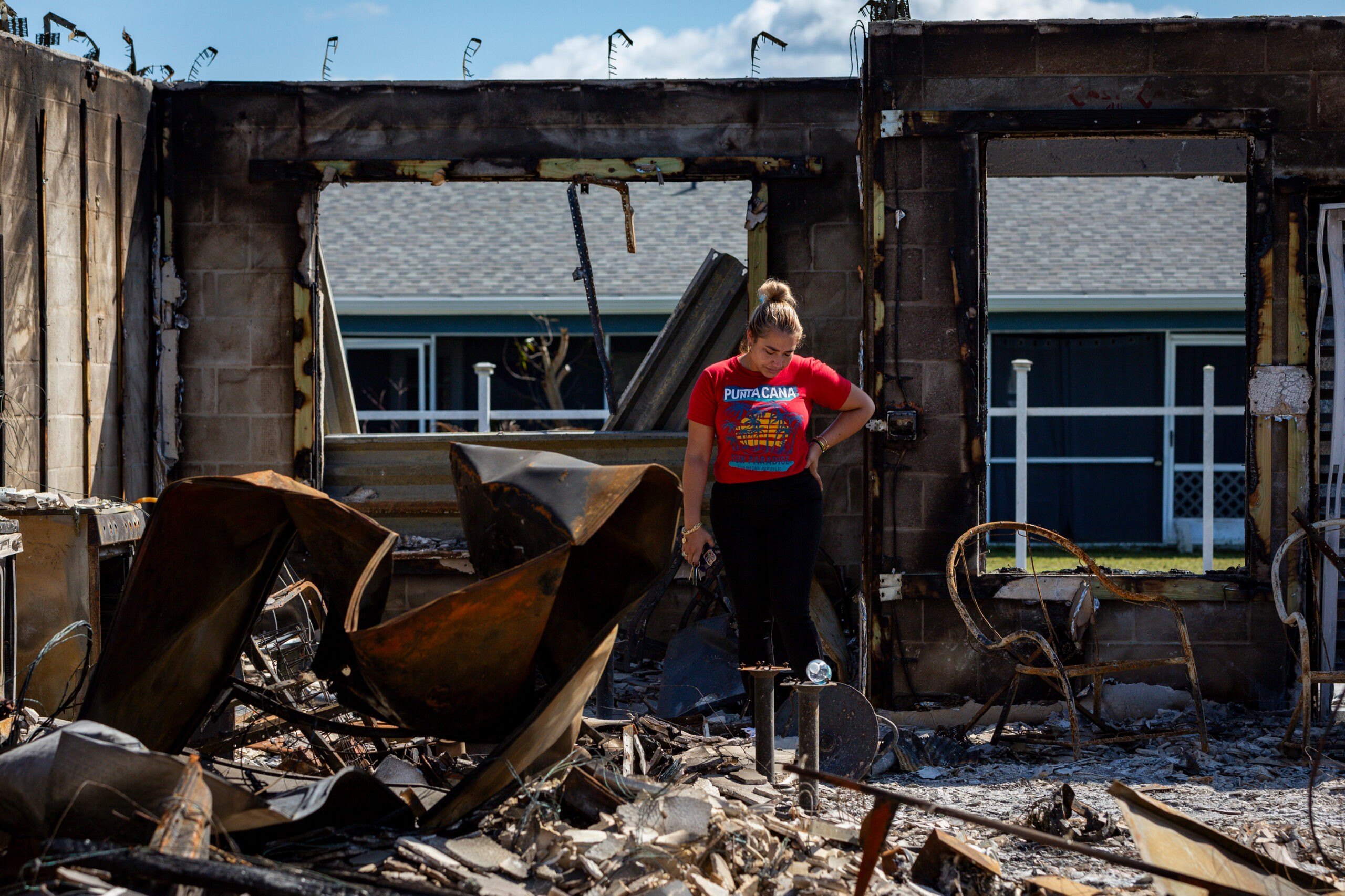A person in a red tee shirt looks at their burned-out home after Hurricane Milton's landfall