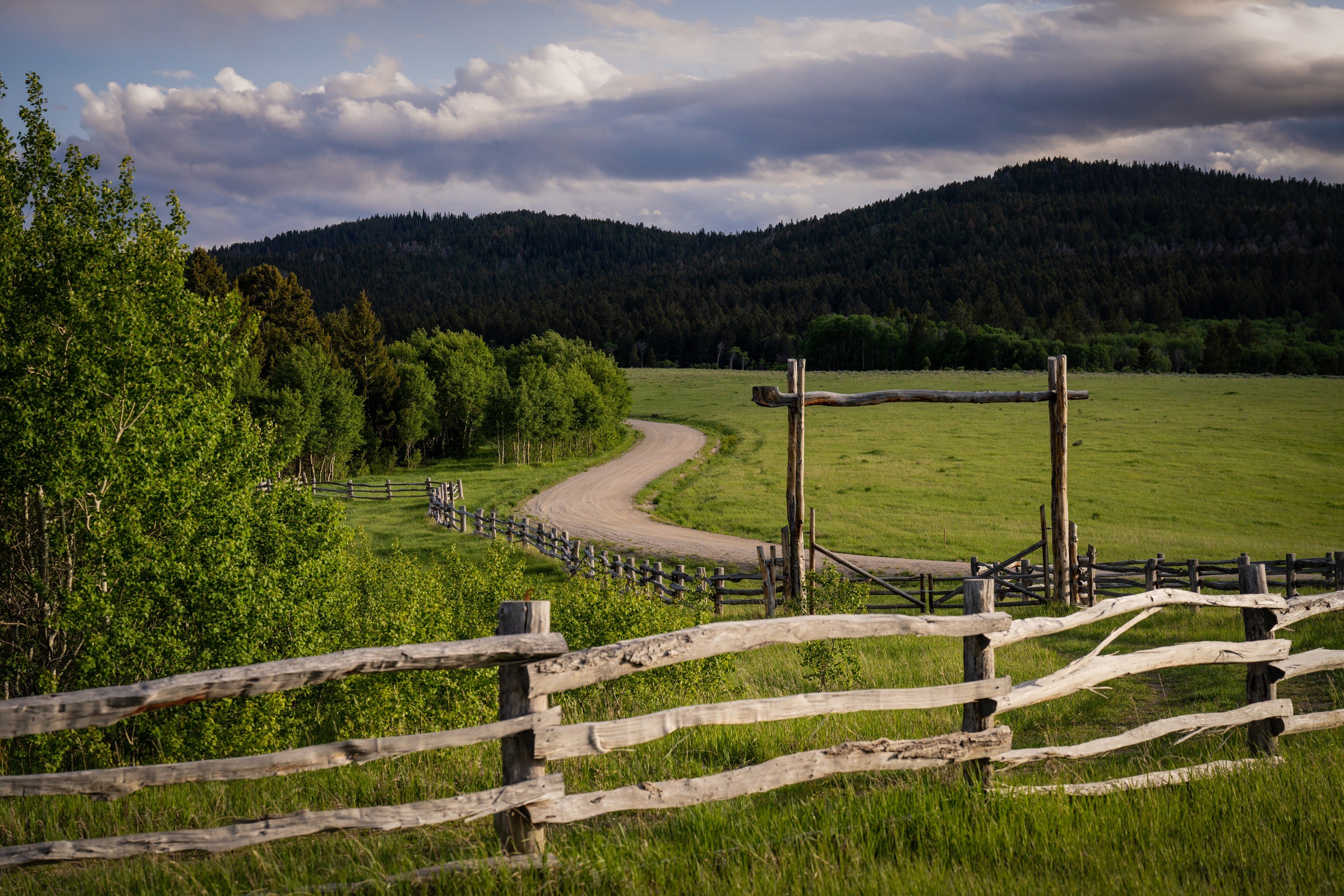 A wooden fence and a path are seen against the backdrop of mountains in Teton Valley, ID