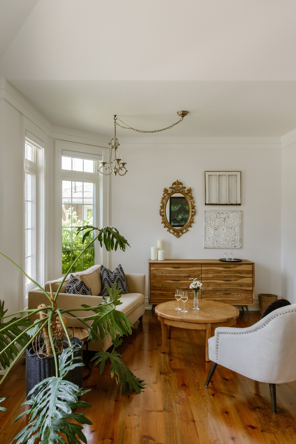 VERTICAL - Bright sitting room area featuring classic hardwood floors, a neutral sofa, and mid-century modern wood furniture.