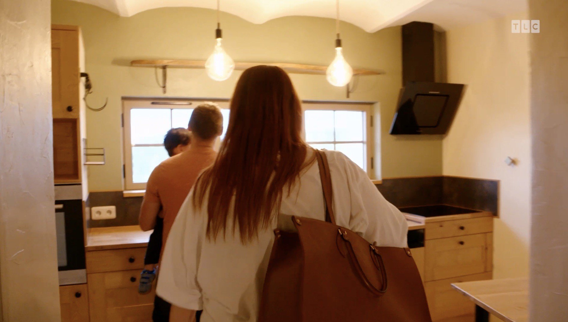 The kitchen is grounded by warm-toned wooden floors and cabinets adorned with black hardware, while a scallop ceiling detail adds some whimsy to the area.