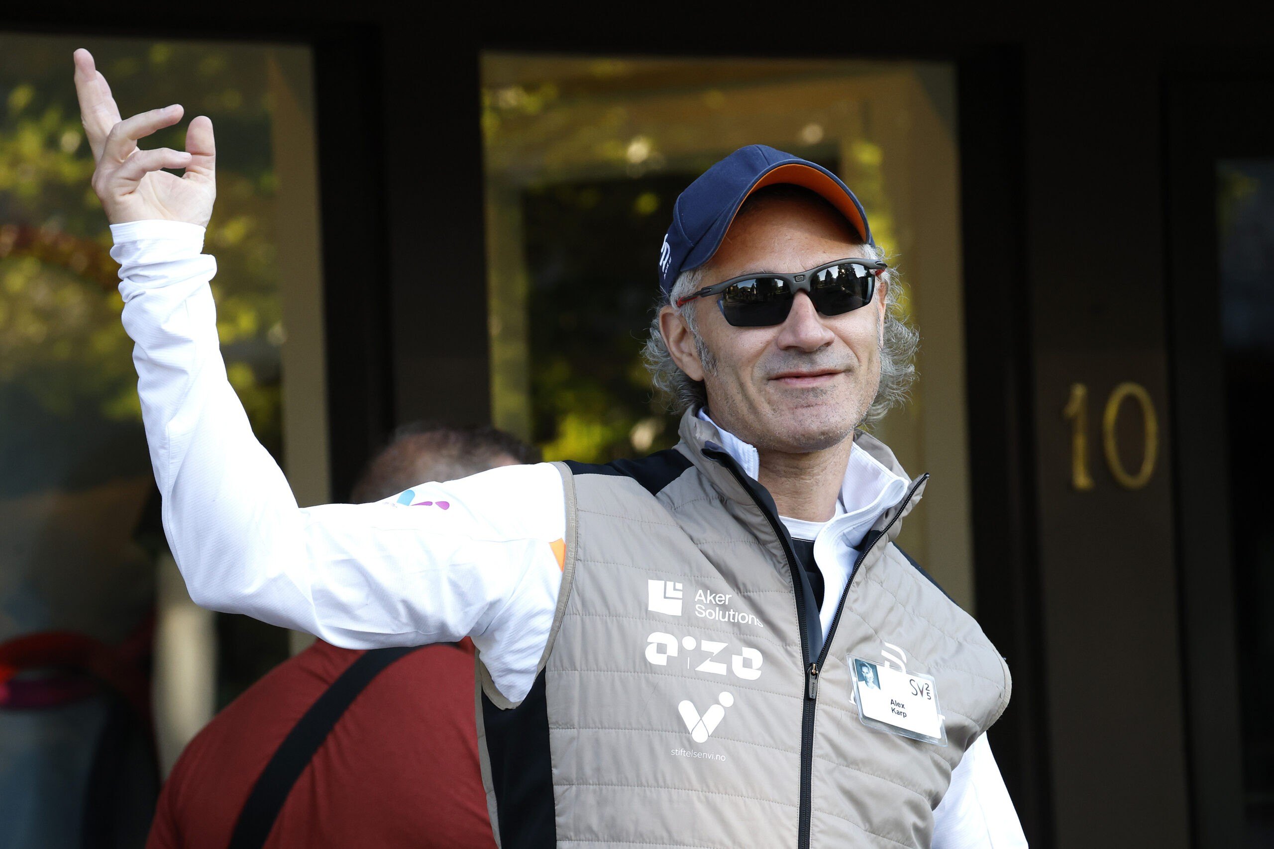 SUN VALLEY, IDAHO - JULY 10: Alex Karp, CEO of Palantir Technologies, talks to members of the media as he walks to a morning session at the Allen & Company Sun Valley Conference on July 10, 2025 in Sun Valley, Idaho. Every year, some of the world's wealthiest and most powerful figures from the media, finance, technology, and political spheres converge at the Sun Valley Resort for the exclusive week-long conference hosted by boutique investment bank Allen & Co. (Photo by Kevin Dietsch/Getty Images)