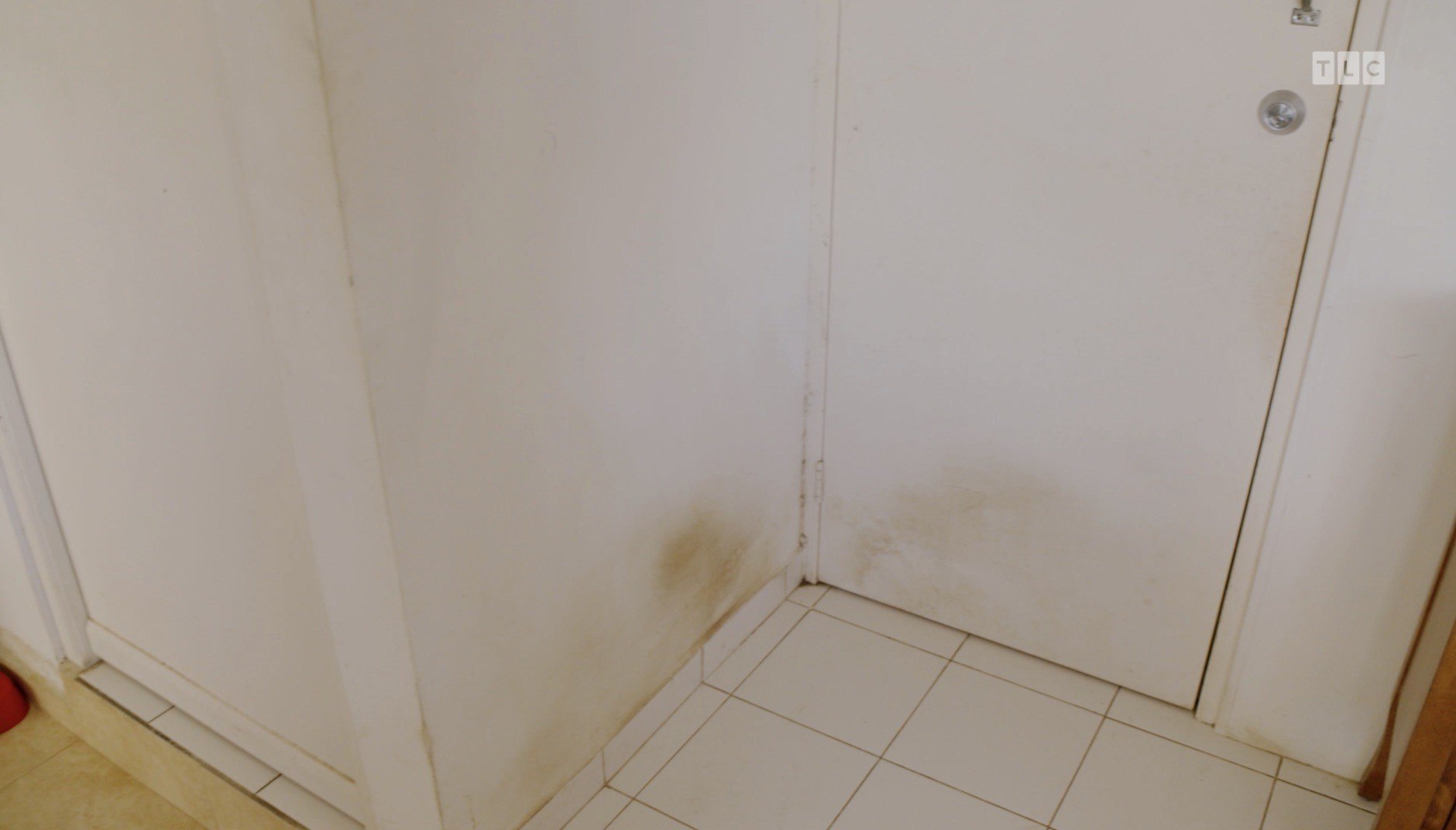 Several stains are visible at the base of the walls and doors, and on the white square tile floors.