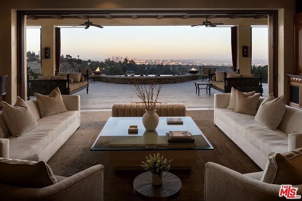 Elegant modern lounge showcasing clean white sofas, a glass-top coffee table, and stunning skyline views at sunset.