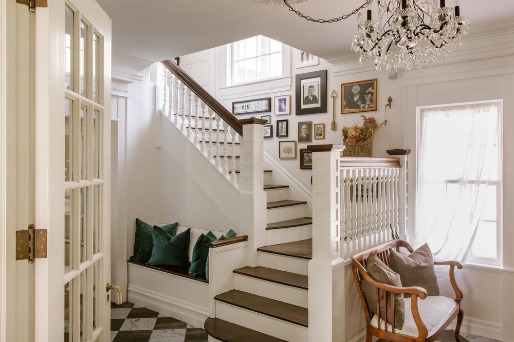 Stately entryway and foyer displaying a grand wooden staircase, built-in bench seating, checkered tile floors, and a gallery wall of framed portraits.