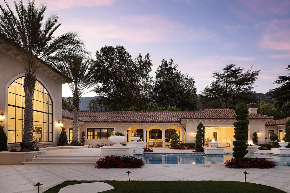 Twilight view of the back patio and pool area showcasing arched loggias, palm trees, and warm exterior lighting.