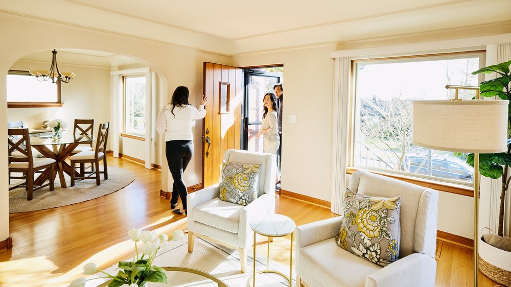 Wide shot of couple walking through front door of home for sale with real estate agent during open house