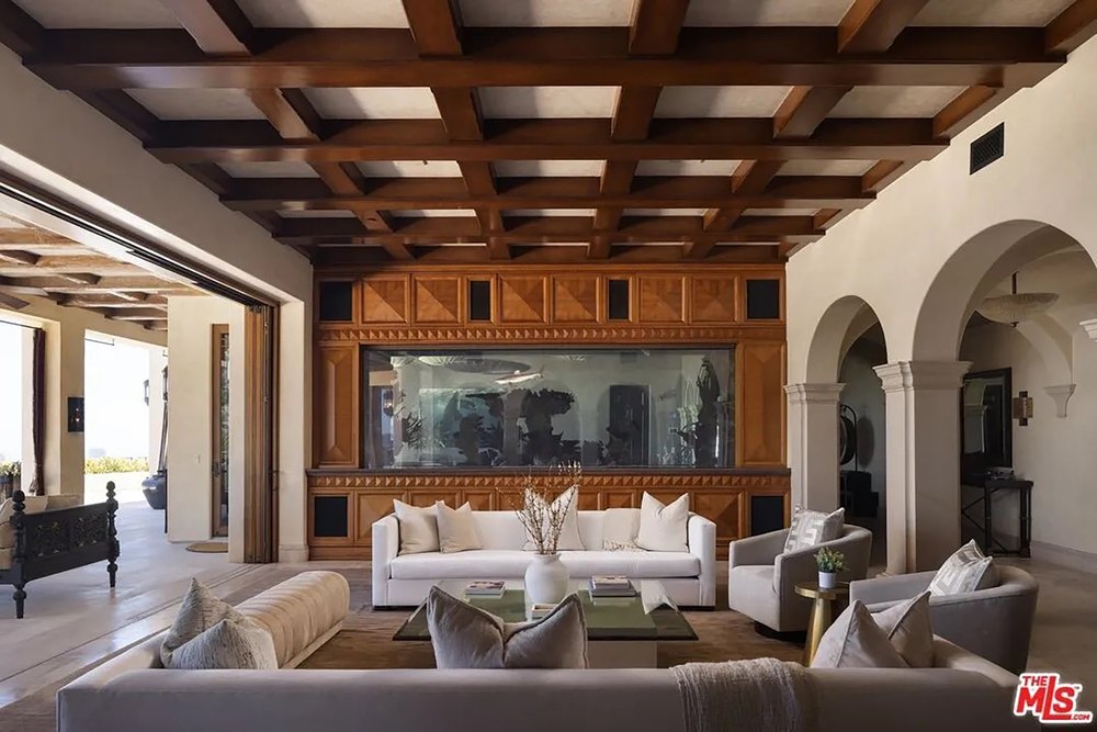 Grand open-concept living area with a large aquarium backdrop, coffered wood ceilings, and white sofas.