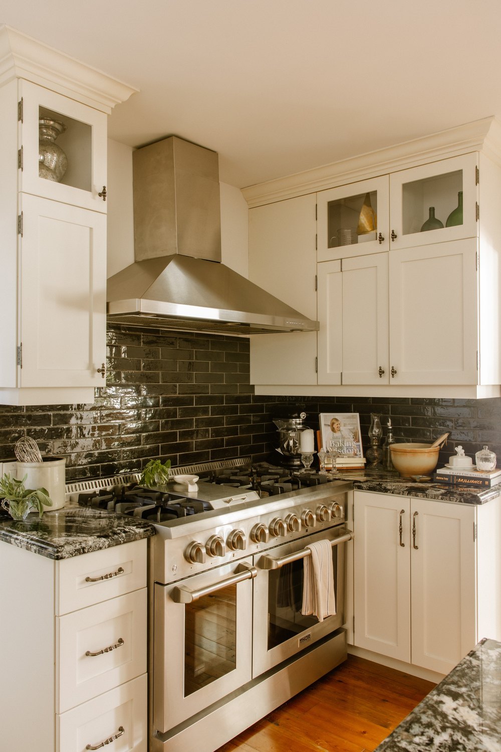 VERTICAL - Gourmet kitchen setup featuring a large stainless steel gas range, dark glossy subway tile backsplash, and white cabinetry.