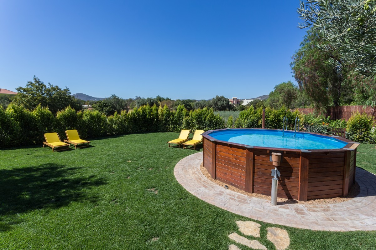 An above ground pool sets on a concrete pad in the backyard on a sunny summer day.