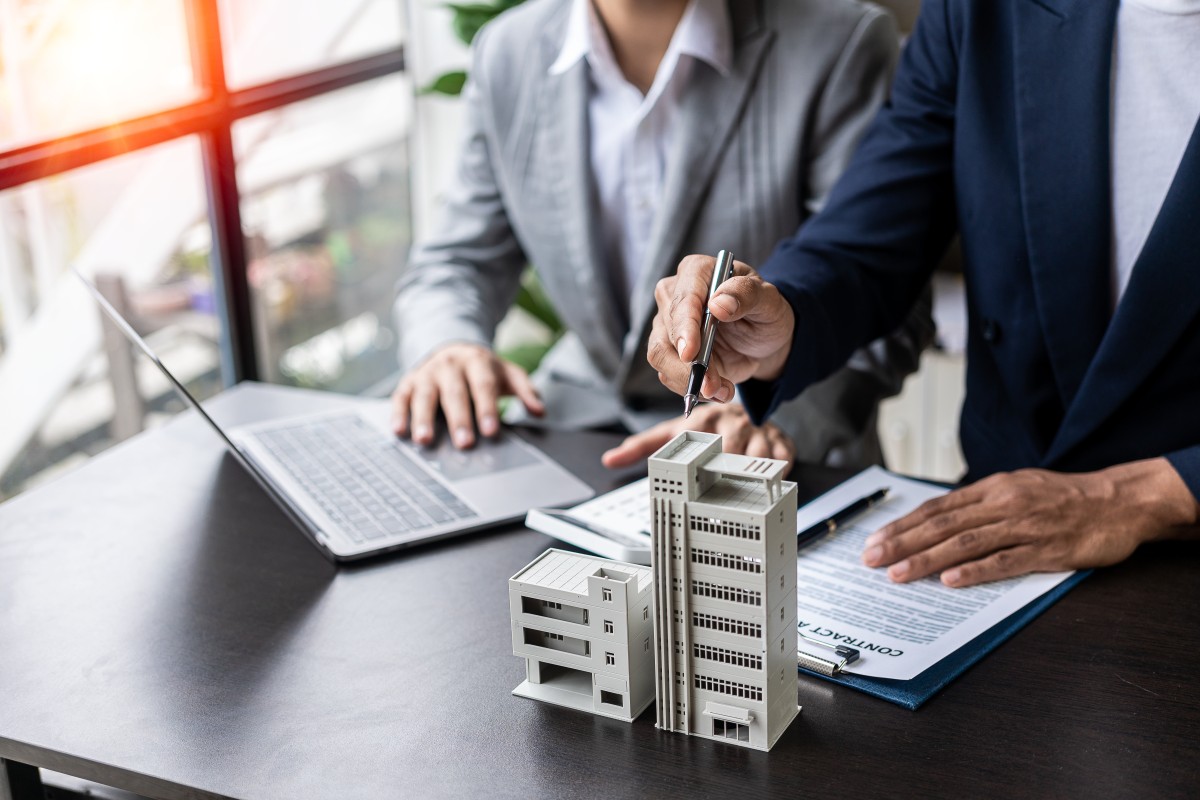 Businessman holding model small building house with property insurance at table in home sales office