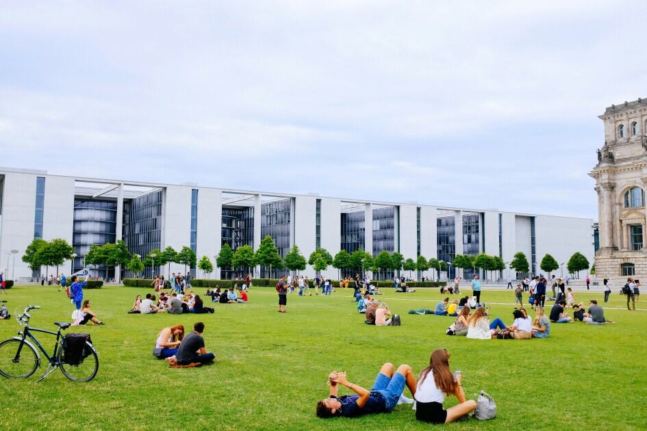Proximity to campus amenities and common areas can be a pro of living on campus vs. off campus. Students sit on a large campus green space in groups across the lawn.