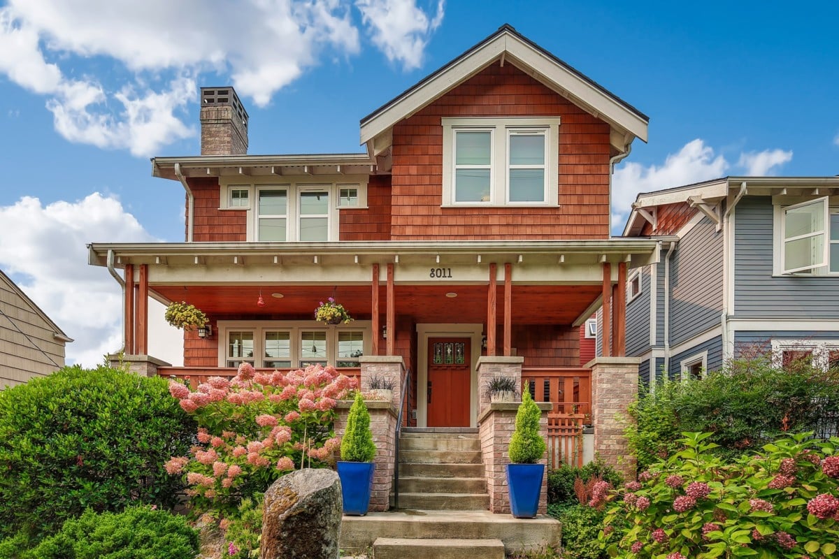 Two-story red brick colored craftsman style home with greenery