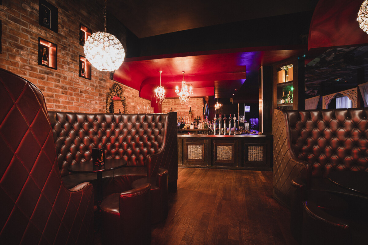 Empty room shot of a nightclub at night. You can see the bar and the drinks in it and the empty chairs.