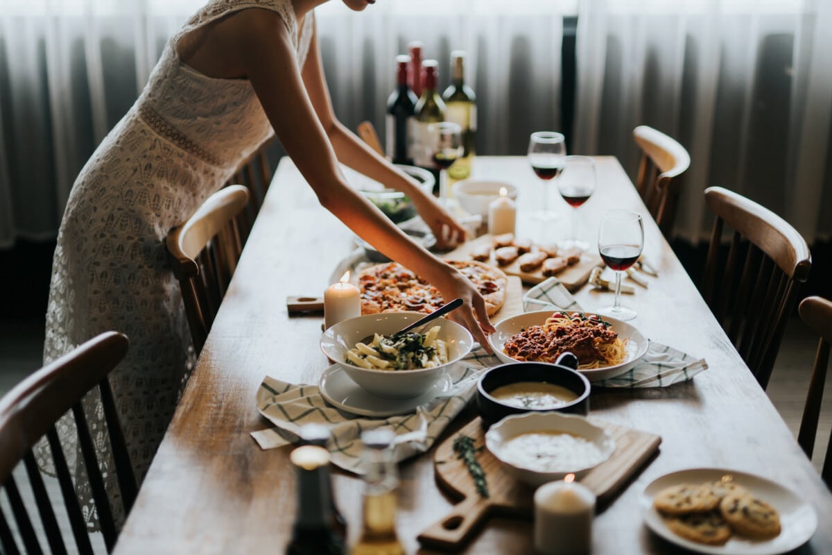 Young woman setting the table and serving food and wine ready for party with friends at home