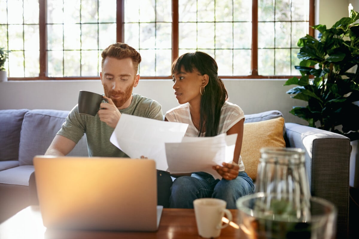 Shot of a couple going through paperwork while using a laptop at home