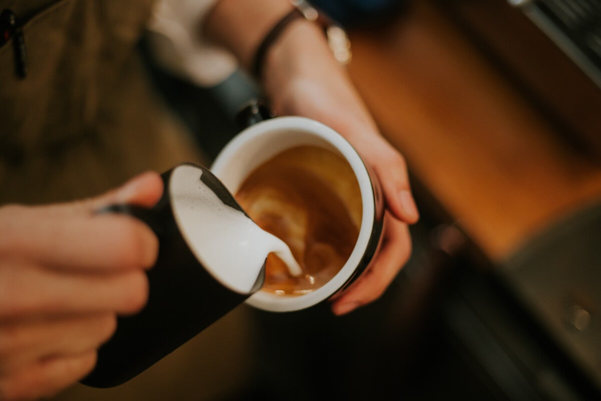 Close-up of barista hand while making frothy drink menu