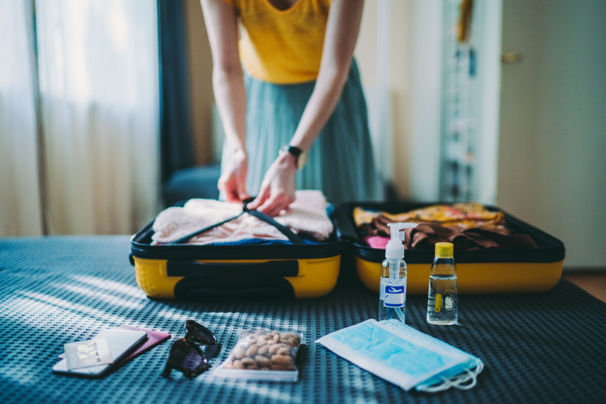 Woman packing suitcase for summer trip, including face masks and travel-sized antibacterial hand gels