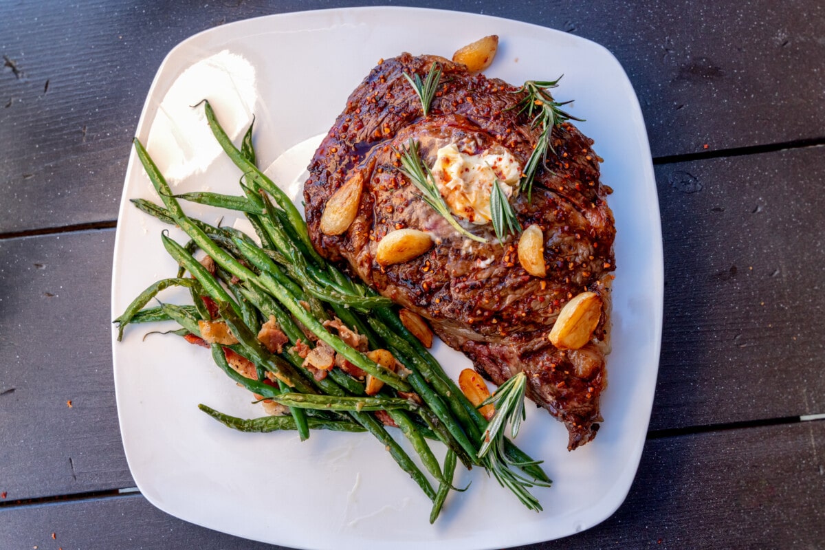 Charcoal Grilled Ribeye Steak Medium Rare Plated With A Side Of Sauteed Green Beans With Bacon And Garlic