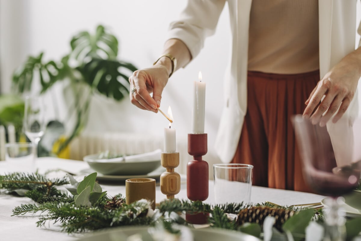 Unrecognizable female hands lights the candle on Christmas table in dinning room.