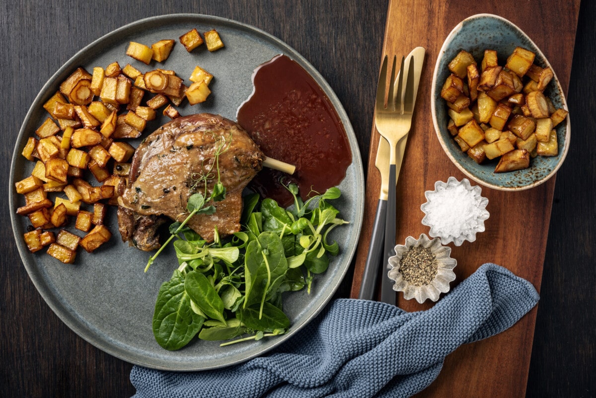 Duck confit with potato and parsnip chips and sauce in a skillet ready for serving. Overhead view, horizontal format with some copy space.