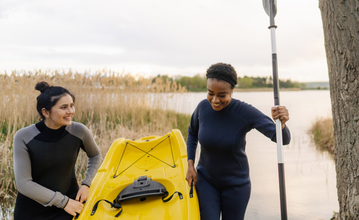 two women holding a yellow kayak in front of a lake