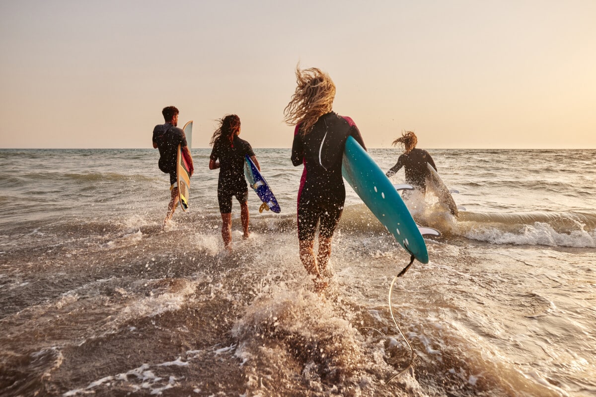 four friends running into the ocean with their surfboards