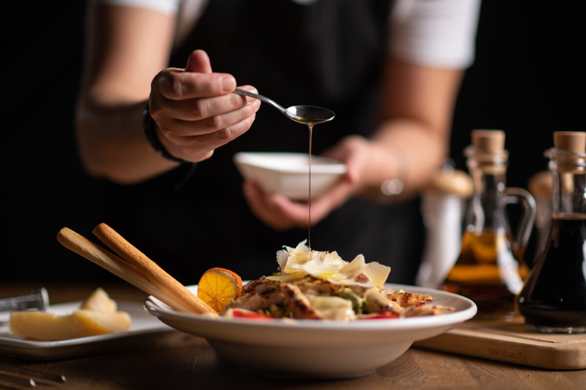 A female chef pouring sauce from the spoon on meal on a black background.