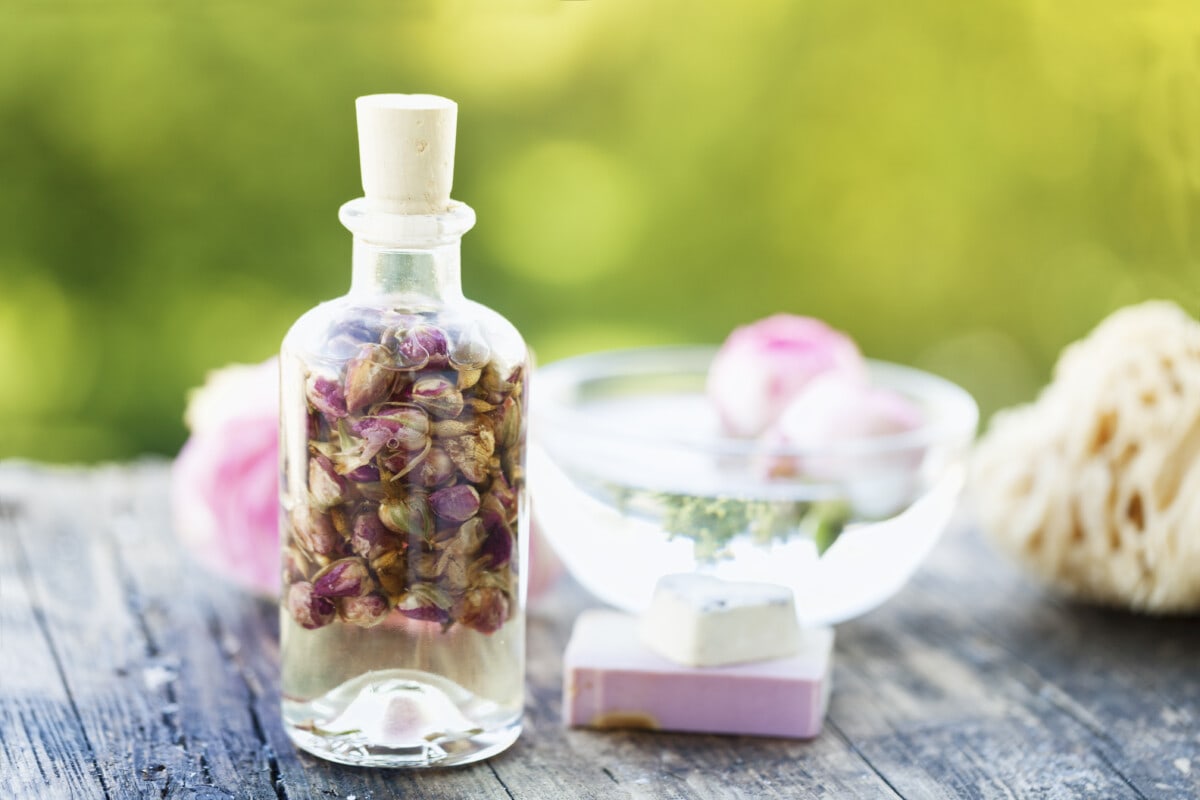 glass bottlel with massage oil with dried rose buds, soap bar and a pink rose on rustic weathered wood