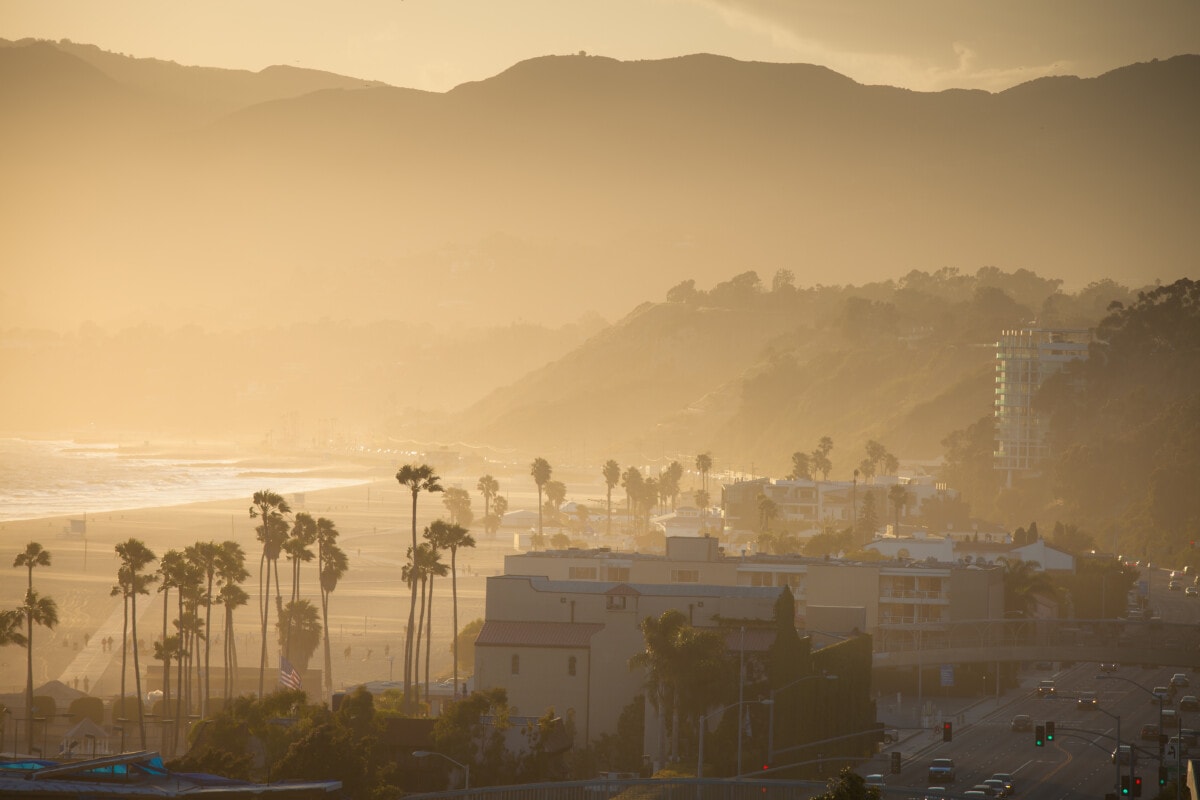 Northern Santa Monica with Pacific Coast Highway (Interstate 1) in the right foreground, with Pacific Palasades, Malibu, and the Santa Monica Mountains rising in the background. The Pacific Ocean can be seen to the left of Will Rogers State Beach in the middleground.