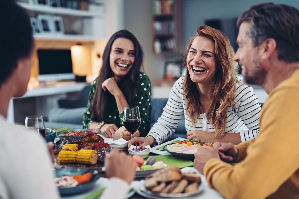 Group of friends sitting around a table at home, eating, drinking and talking