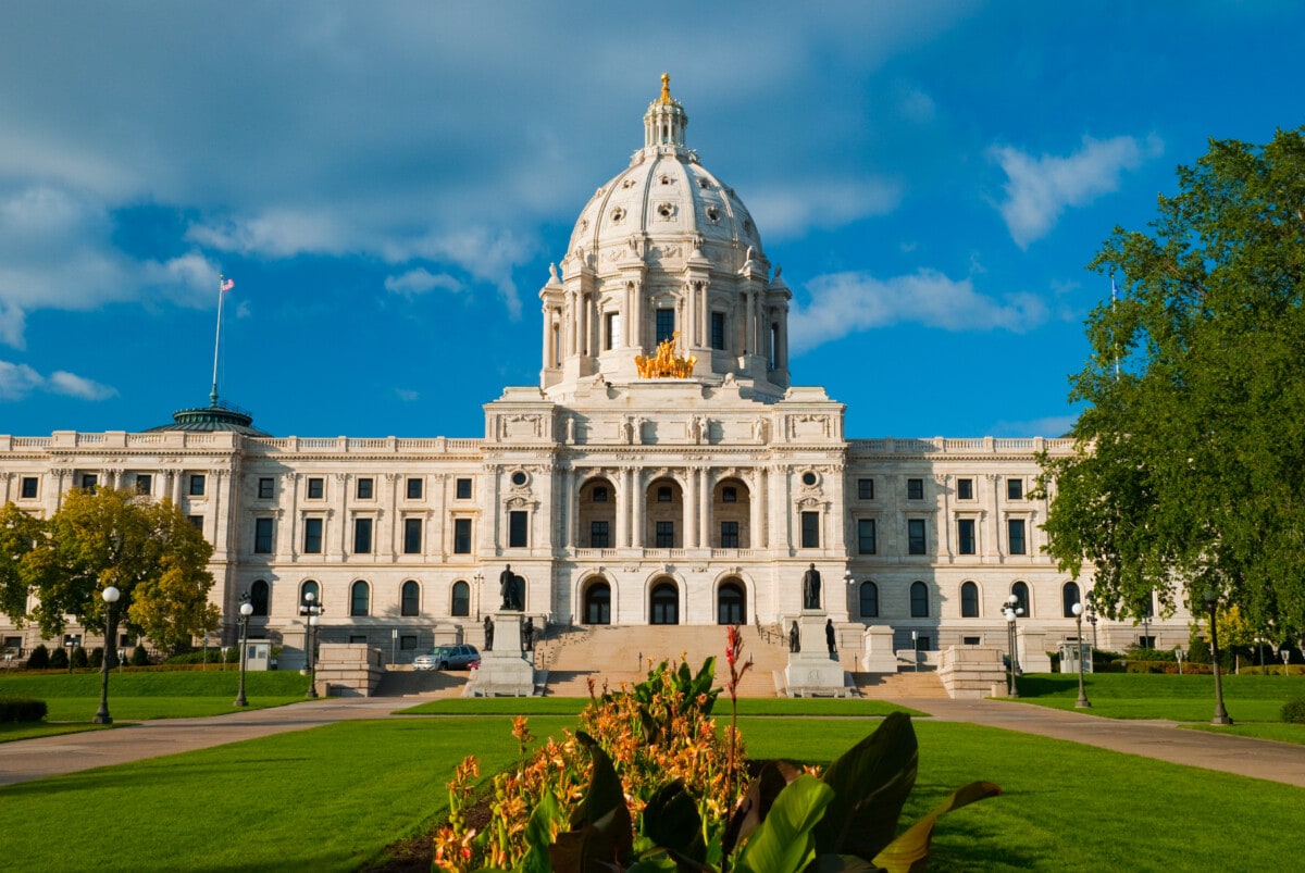 "Front view of the Minnesota State Capitol Building (the center of the State Government of Minnesota) in St. Paul, with a lawn, plants, and flowers in the foreground. The Minnesota State Capitol building was designed by Cass Gilbert with Italian Renaissance and Beaux Arts influences."