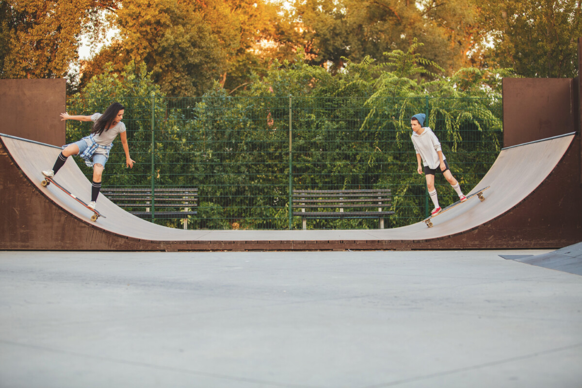 Two young women are skating down in bowl in skateboard park. They are practicing their skateboard skills.