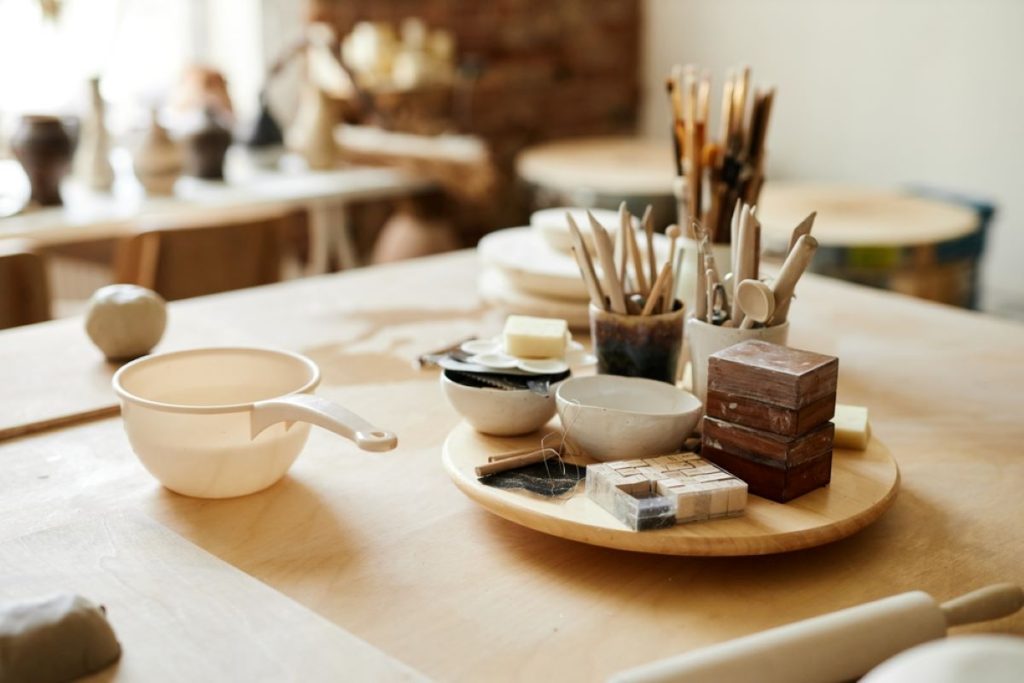 Organized pottery tools sit on a wood table with balls of clay ready to be shaped.