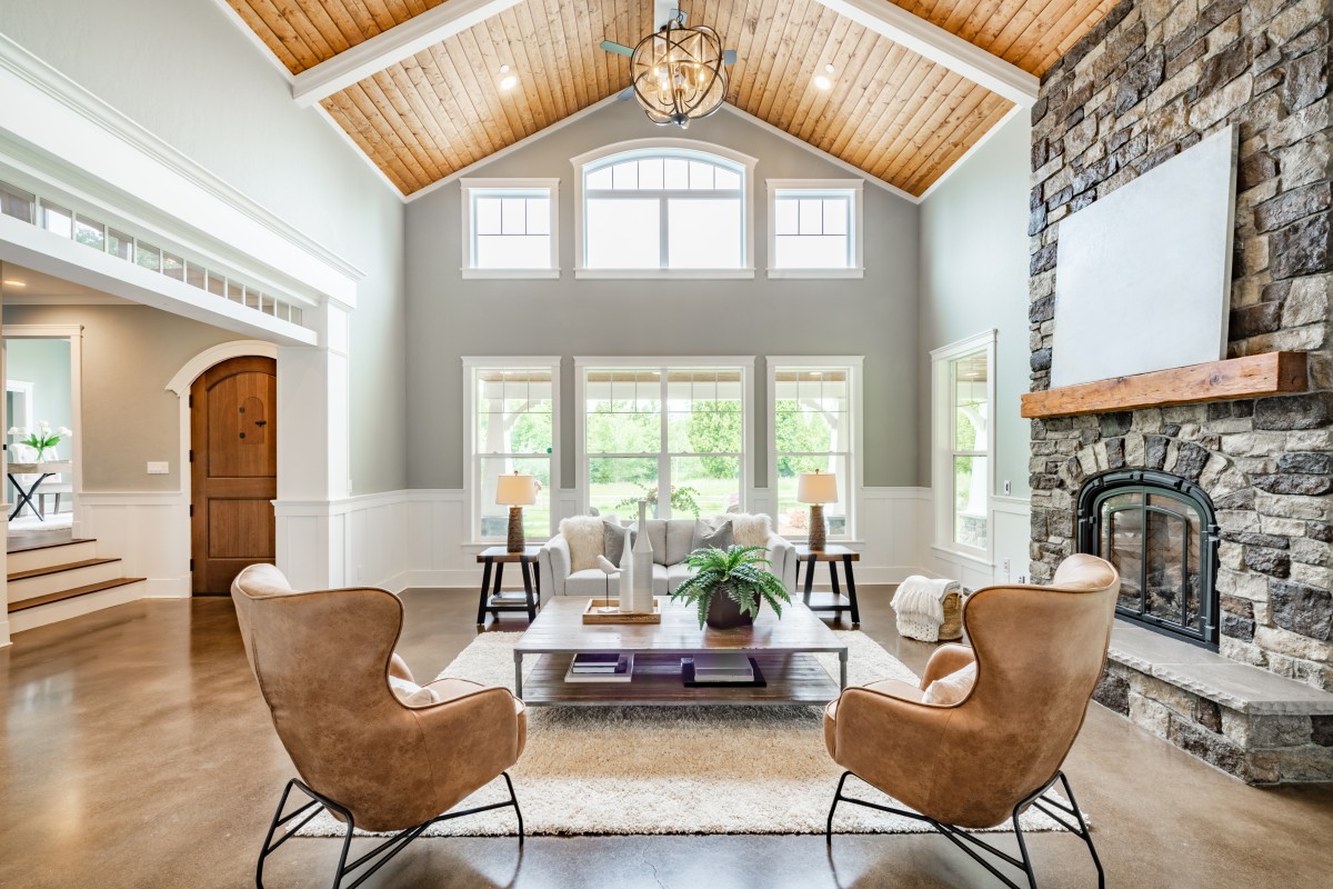 Living room interior with vaulted ceiling with wood cedar panelling stone fireplace brown leather armchairs coffee table and area rug natural brown tones