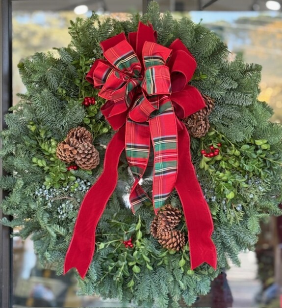 An evergreen wreath with pinecones and a large red bow
